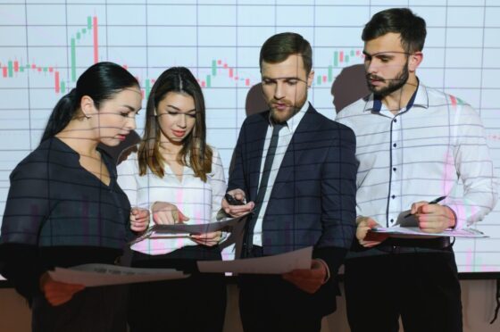 Group of business people working at modern office.Technical price graph, red and blue candlestick chart and stock trading computer screen background. Double exposure. Traders analyzing data